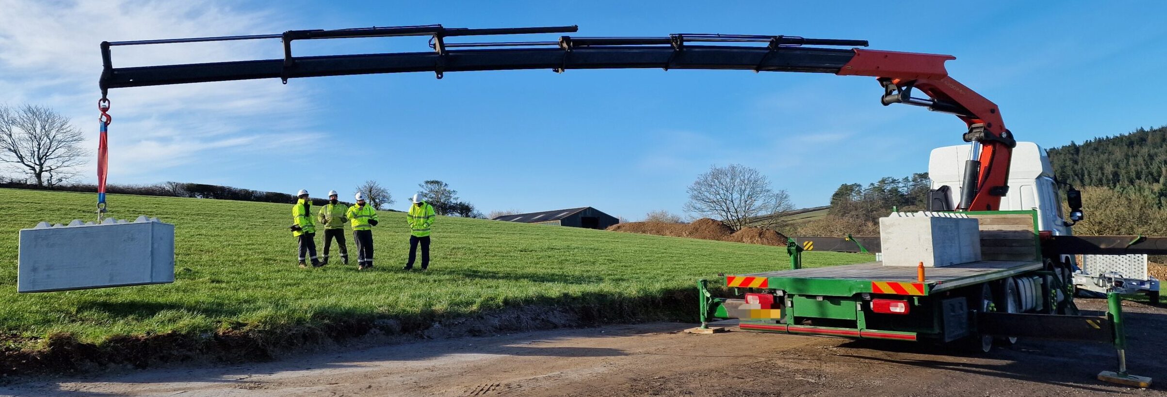 Lorry mounted crane lifting a concrete block in a field. Blue sky and sunshine.